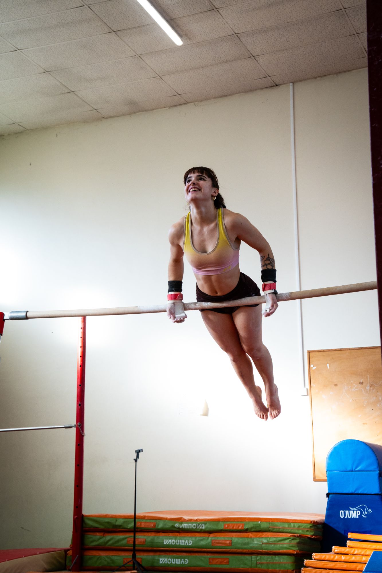 Gymnaste souriante en appui sur une barre, pendant un entraînement de gymnastique