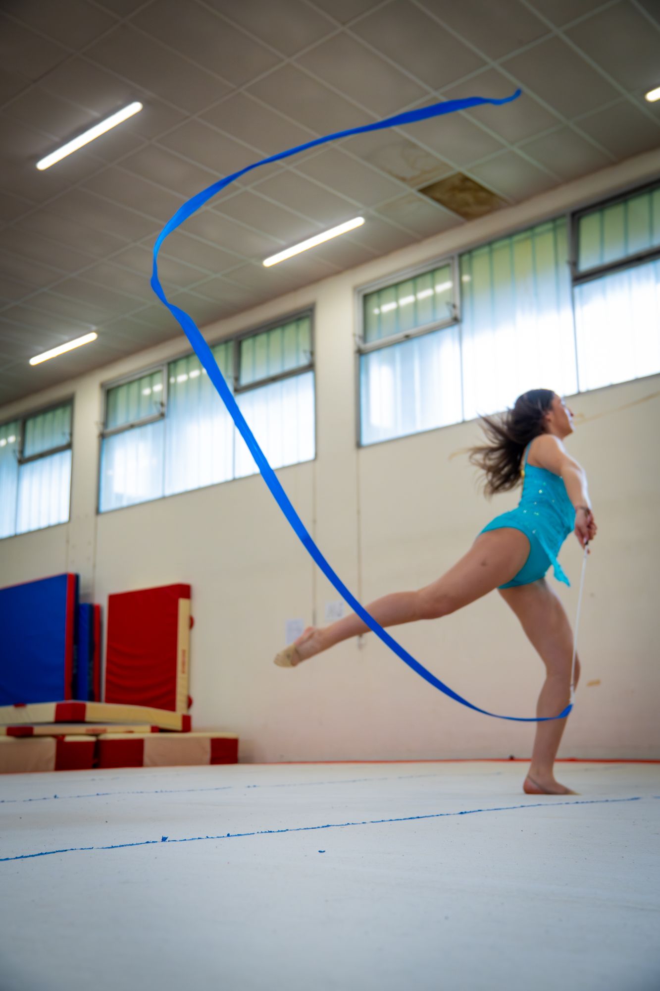 Gymnaste en justaucorps turquoise faisant onduler un ruban bleu, en gymnastique rythmique