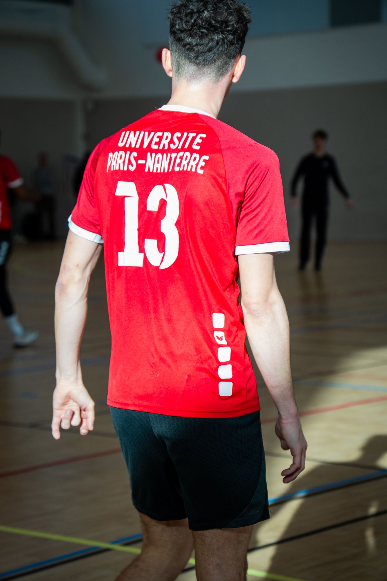 Joueur de dos, maillot rouge numéro 13 floqué Université Paris-Nanterre, dans un gymnase