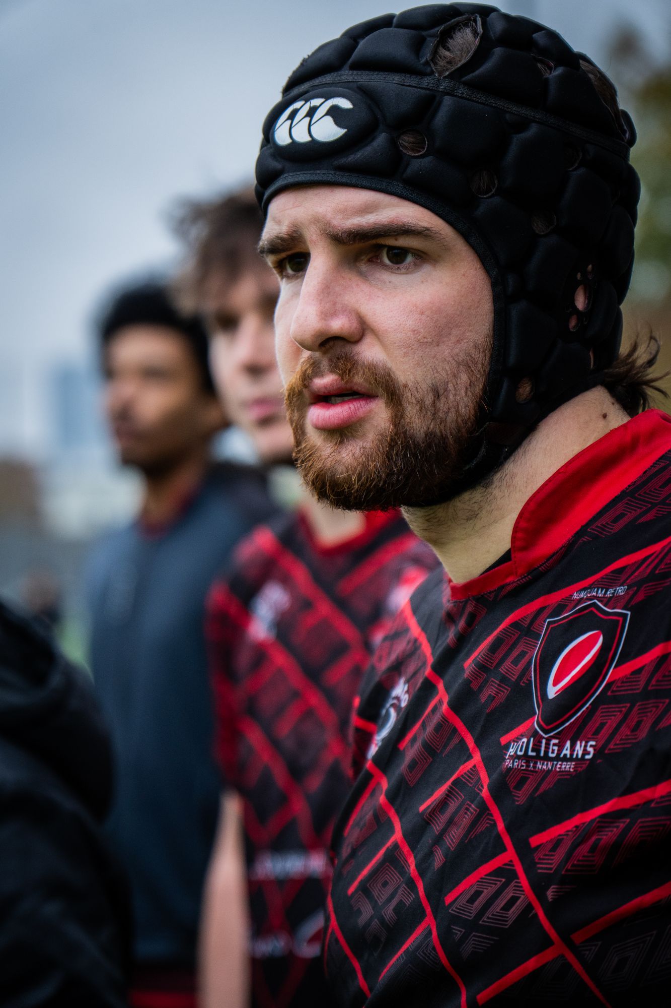 Joueur de rugby coiffé d’un casque, concentré au bord du terrain avec ses coéquipiers